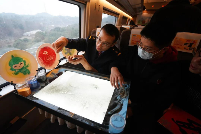 1月15日，在江苏南京开往福建平潭的G1605次列车上，旅客体验沙画创作。季春鹏摄（新华社）
