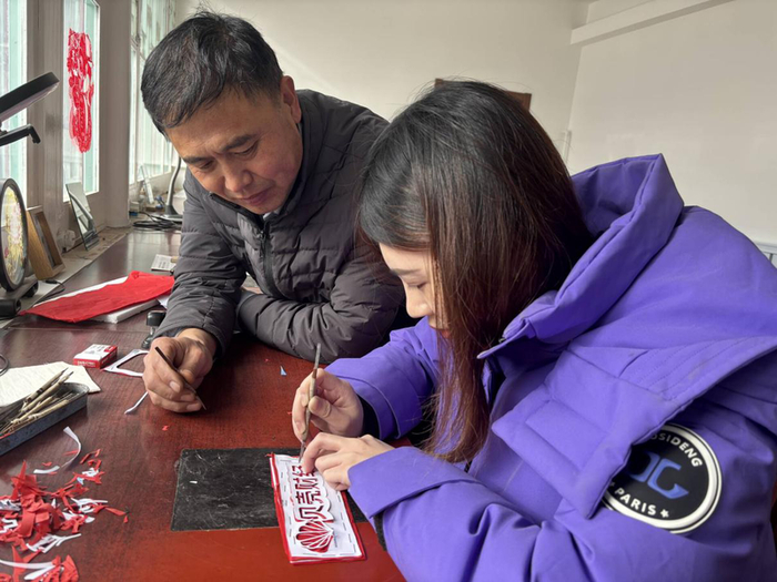 焦新胜指导记者体验刻剪纸的过程。 焦氏剪纸工作人员 摄