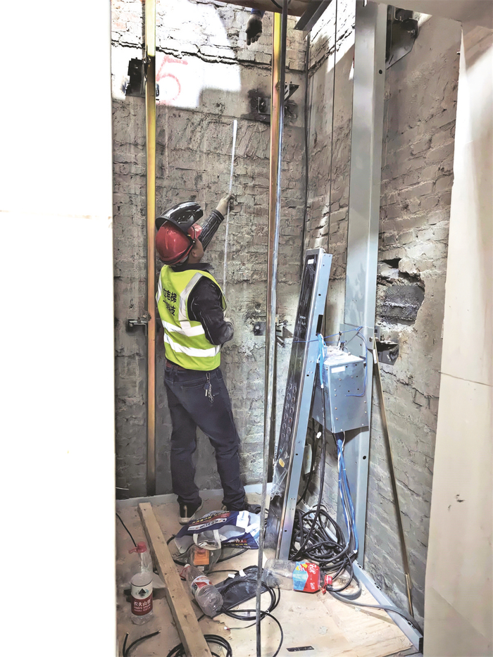     在一居民楼电梯井，施工人员进行电梯更新施工作业。