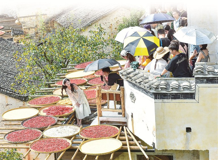 江西省上饶市婺源县江湾镇篁岭村，游客在摆放辣椒、南瓜等农作物的晒台前拍照打卡。资料图片