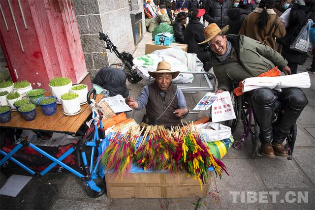 图为普琼（左）正与同伴一起在八廓商城南门售卖“罗萨梅朵” 摄影：赵振宇