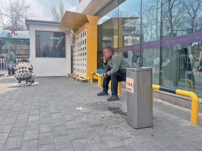 3月28日，首都儿科研究所附属儿童医院东门，家长坐在灭烟处旁吸烟。新京报记者 王飞 摄