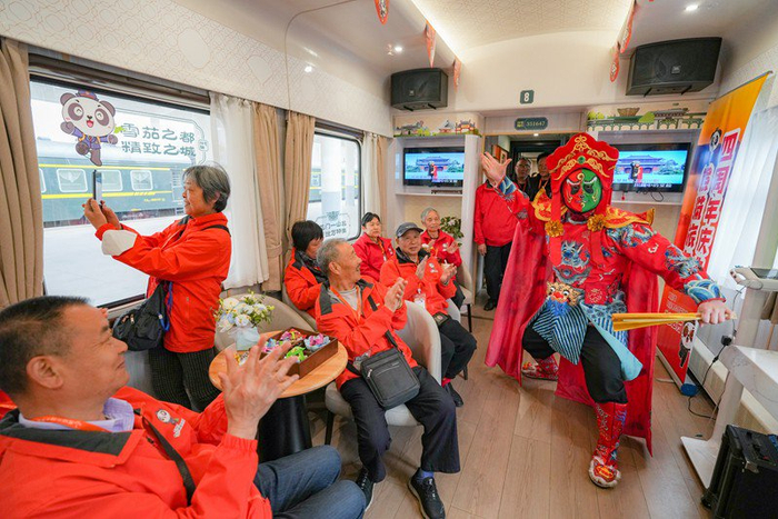 3月28日，在Y471次“熊猫专列·什邡号”列车上，旅客们在观看川剧变脸表演。新华社记者 王曦 摄