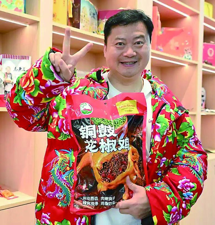     “卤鹅哥”林江穿着大花袄，手拿荣昌特产。▶