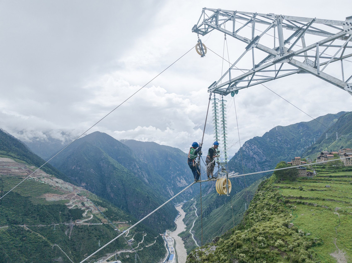 电力工人在高山峡谷间搭设输电线路。 国网四川阿坝州电力有限责任公司供图