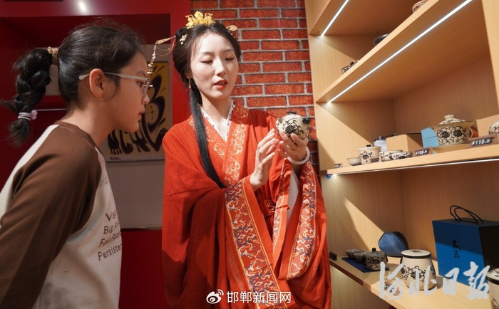 5月1日，邯郸成语之都·文创旗舰店内，身穿战国袍的工作人员（右）为顾客介绍磁州窑茶具。 河北日报记者 陈正摄