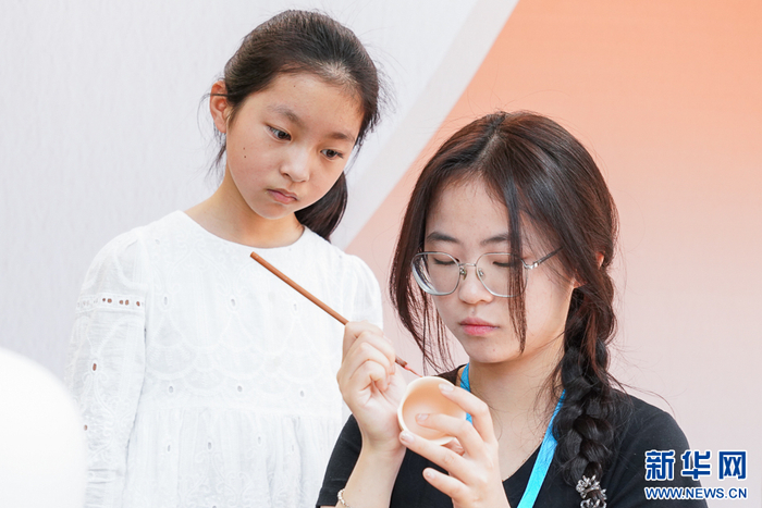   5月2日，在泉州工艺美术职业学院展区内，小游客观看瓷艺勾线作业。新华网 肖和勇 摄