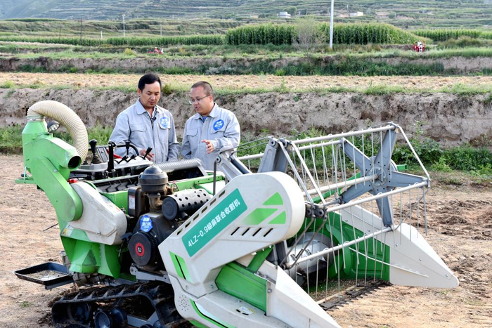 　　戴飞（右一）检查胡麻联合收割机。（受访者供图）