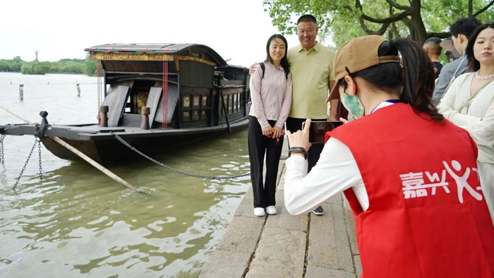 5月4日，在浙江省嘉兴市南湖景区湖心岛，嘉兴义工协会义工为游客提供拍照服务。新华社发（金鹏摄）