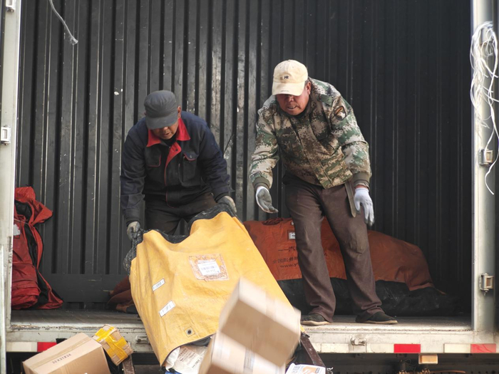 两名工作人员将快递包裹倾倒在分拣设备上（记者江晓晨  摄）