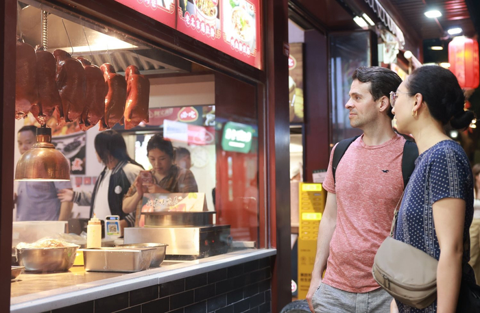 5月16日，南锣鼓巷，外国游客透过橱窗观看烤鸭的切片过程。