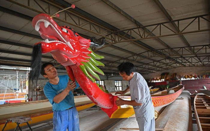↑汨罗市屈子祠镇九子龙屈原龙舟厂内，两名工人一起给龙舟安装龙头。新华社记者 李尕 摄