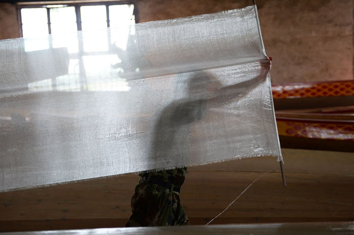 ↑汨罗市屈子祠镇九子龙屈原龙舟厂内，一名工人正在准备制作龙舟用的玻璃纤维布。新华社记者 陈振海 摄