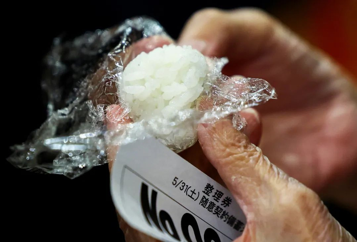 5月31日，在日本东京的一家超市，一名顾客手持用储备米煮的饭团/图源：新华社