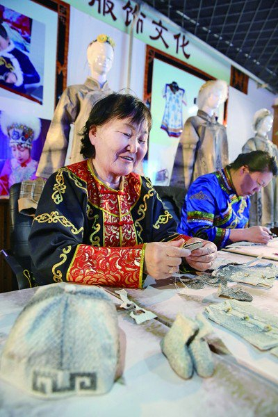     国家级非遗赫哲族鱼皮制作技艺代表性传承人尤文凤（左）在用鱼皮制作民族服饰。本报记者 闫汇芳摄