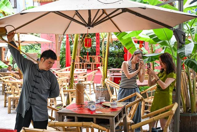 6月8日，在重庆市渝中区山城巷的一家露天茶馆，茶艺表演者与游客互动。新华社记者 王全超 摄