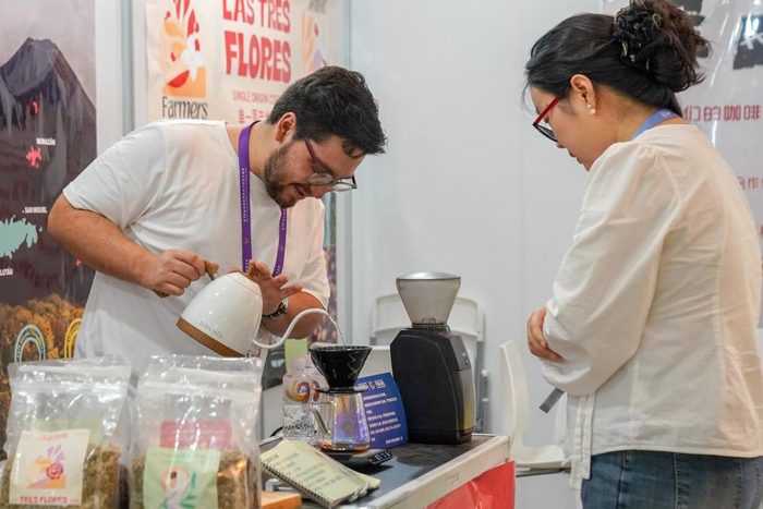 6月20日，来自萨尔瓦多的参展商（左）在咖啡产业馆为顾客冲咖啡。 新华社发（彭奕凯 摄）