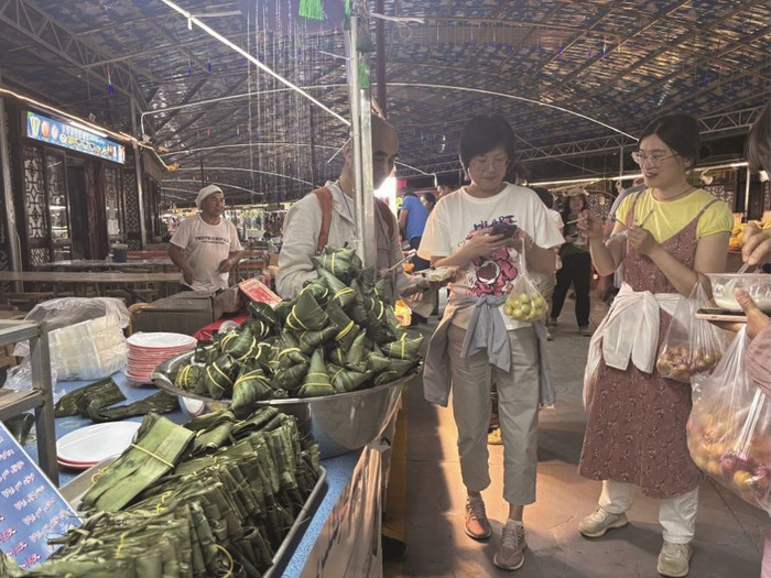 图为游客正在库车市乌恰供销大巴扎夜市购买酸奶粽子