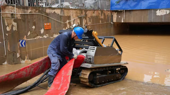 电力工作人员正在给排涝机器人接上排水管，准备为地下停车场排涝。