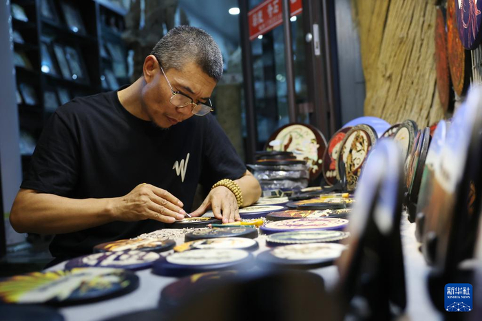 6月26日晚，敦煌夜市的一名经营者在摊位上制作敦煌特色文创产品。新华社记者陈斌摄