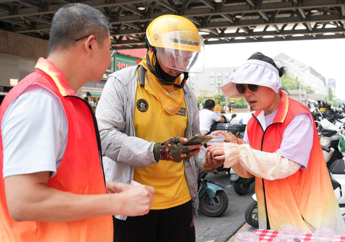 　　6月25日，在北京市东城区崇外街道一处“暖新驿站”外，街道工作人员（右）为一名外卖员送上冰镇饮料。新华社记者 鞠焕宗 摄