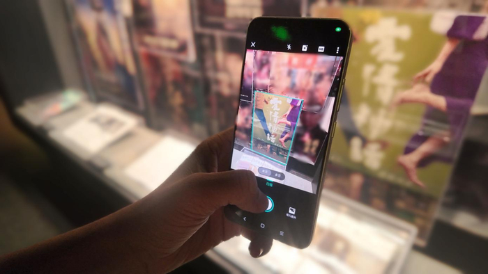 图说：参观者用扫描全能王App“智能高清滤镜”功能对《爱情神话》海报图像进行切边矫正