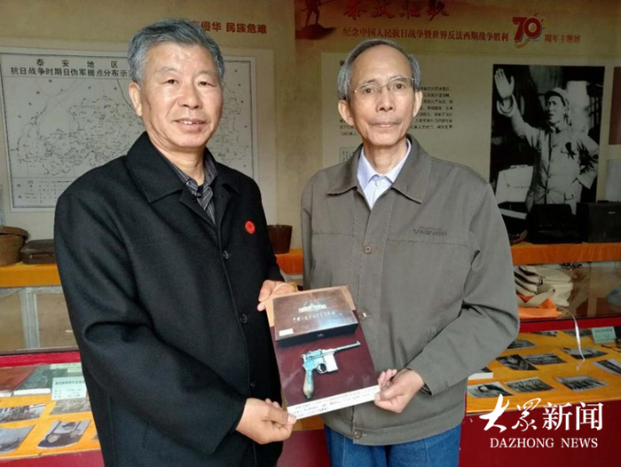 原泰安市委党史办调研员宋元明从林水星（右）手中接过手枪照片。