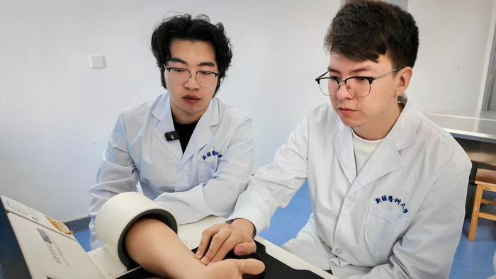　　5月9日，卡力别克·叶尔波森（右）在新疆医科大学使用脉象模拟仪器练习脉诊（手机照片）。新华社记者 王泽宇 摄
