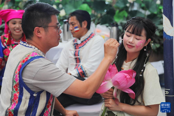 7月14日，在昆明南站候车大厅举行的“花脸节”活动中，工作人员为游客画花脸。新华社发（杨紫轩摄）