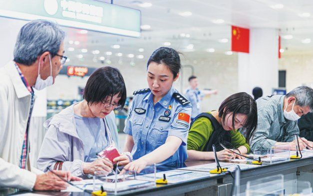 图为在大连周水子国际机场入境大厅，大连周水子边检站民警（左三）帮助外籍旅客填写入境卡。 新华社发