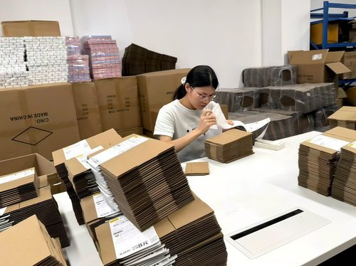 图：龚琦招聘的助理正在贴快递面单，来自拼多多的订单像书一样厚。