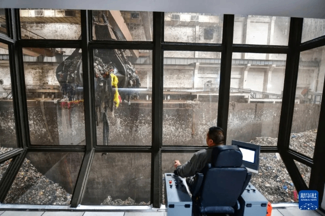 工作人员在控制室内操作设备吊运垃圾。图源：新华社