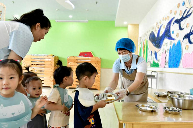 （山东省滨州市博兴县一家幼儿园内，托育班的孩子在排队领餐。图片来源：新华社）