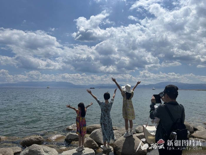 8月6日，几名游客站在赛里木湖岸边的石头上拍照打卡。石榴云/新疆日报记者 宋卫国摄
