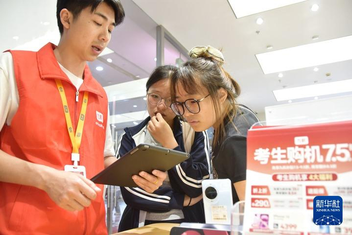 2025年6月23日，云南省蒙自市一商店工作人员为两名今年的高考考生讲解手机以旧换新政策。新华社发（薛莹莹摄）