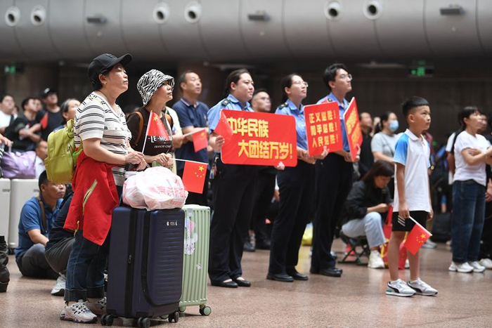 9月3日上午，北京西站，候车厅工作人员为观看转播的旅客分发了五星红旗等物品。新京报记者 王贵彬 摄