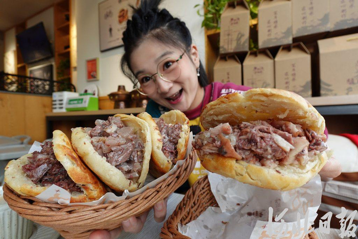北京姑娘小朱（网名“逛吃小猪猪”）在保定打卡驴肉火烧。（河北日报资料片）