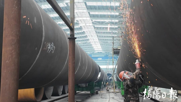 工厂车间内，大型管道林立，工人手持工具对大型管道进行焊接，火花四溅。