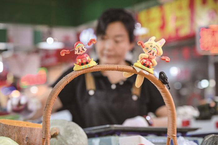 　　在无锡稻香市场，摊主将财神装饰摆上菜篮。