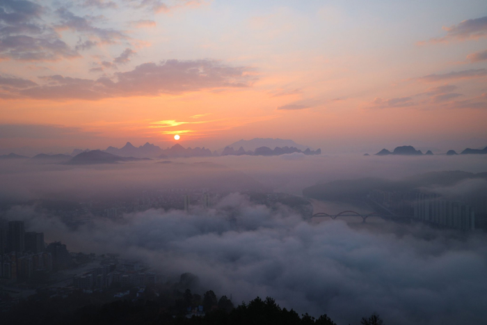 在平乐县平乐镇在云海中若隐若现，朝阳染透天际，与群山共赴一场云雾之约。（平乐县纪委监委供　廖伟高/摄）