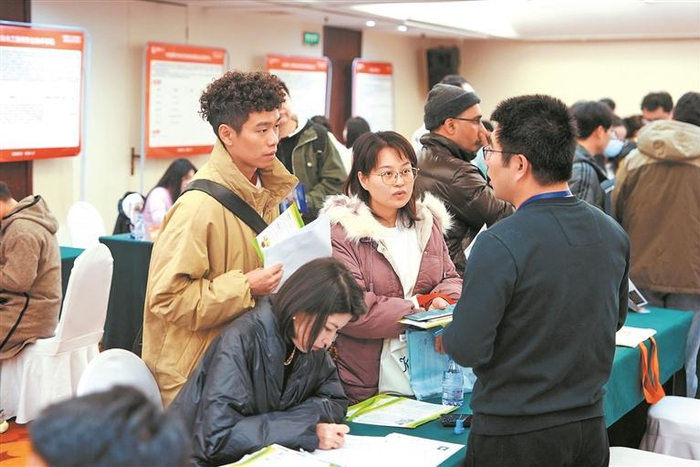 几名学生聚集在招聘展位前，查看岗位资料，并与工作人员交流，细致了解求职信息。