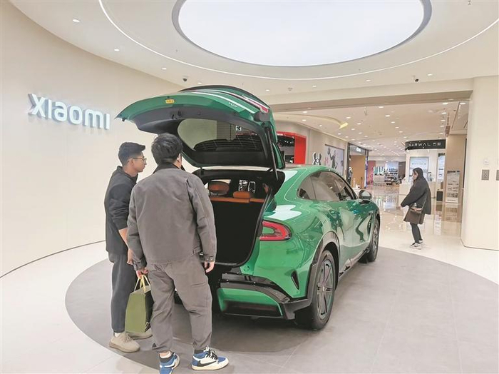小米门店内，消费者围绕展车向工作人员咨询小米汽车相关信息。