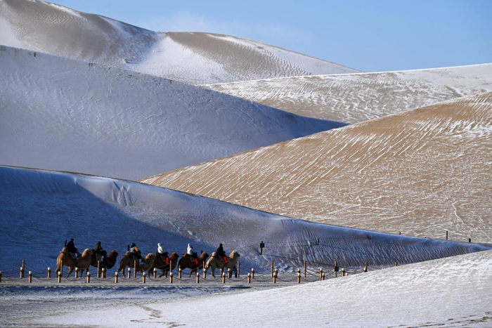 　　游客在甘肃省敦煌市鸣沙山月牙泉景区骑骆驼，观赏雪景。新华社发（张晓亮 摄）