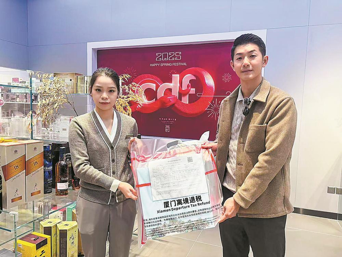     洪伟邦（右）从中华城商场免税店店员手里接过办理好的“一单一包一码”业务商品。王彦雯 摄