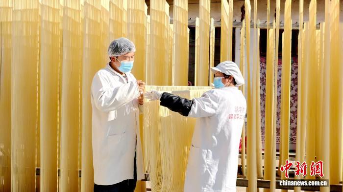 圖為1月初，甘肅隴南市徽縣永寧鎮(zhèn)綠鑫手工空心掛面農(nóng)民專業(yè)合作社內(nèi)，師傅們?cè)诹罆袷止烀?。何?攝