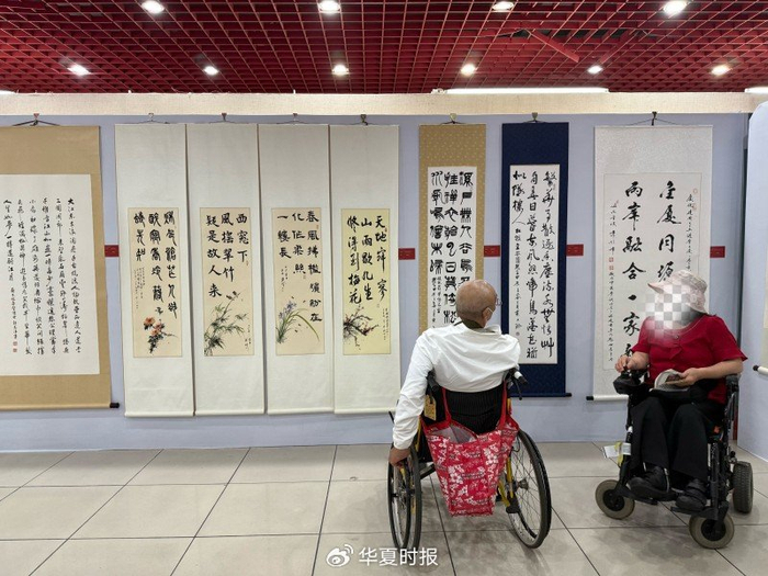 两位残障长者一边欣赏着画作，一边讨论