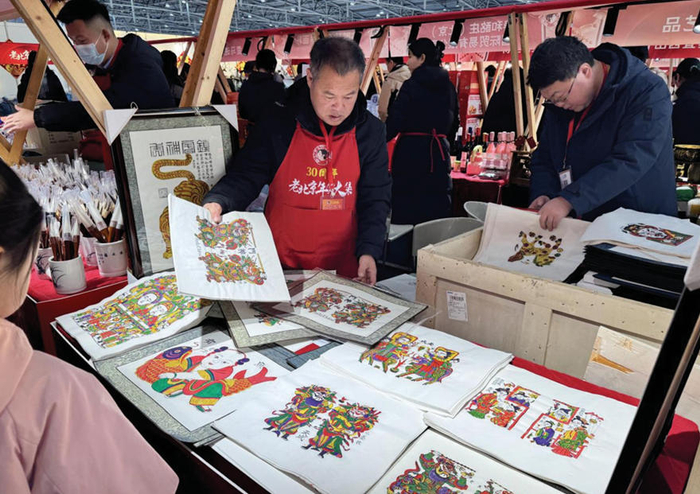 　　图为摊主正在向消费者展示木版年画。