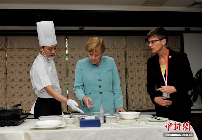 图为默克尔向川菜大厨学习宫保鸡丁的做法。　资料图