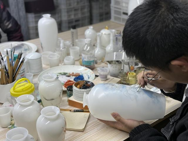 图说：德化一位年轻的画师在工作间为白瓷花瓶画手绘龙纹。