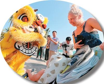 图为近日，在海南三亚，南狮和外国游客零距离互动。